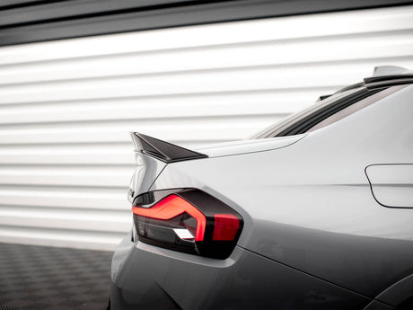 A sleek car's rear with an illuminated taillight and prominent spoiler, parked in front of a white, horizontal-panel garage door.