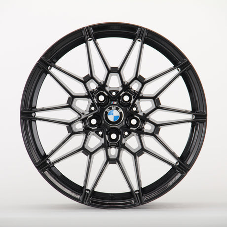 A black, multi-spoke alloy wheel displays a BMW logo at the center, set against a plain white background, highlighting its intricate design.