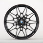 A black, multi-spoke alloy wheel displays a BMW logo at the center, set against a plain white background, highlighting its intricate design.