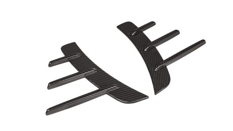 Carbon fiber car parts lie side by side, showcasing aerodynamic fin designs on a white background, highlighting their sleek and modern appearance.