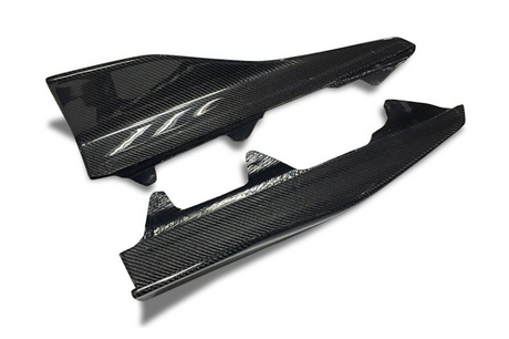 Two carbon fiber car side skirts resting on a white surface. The top piece features a stylized “TT” logo, enhancing its sleek, modern appearance.