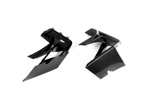 Two angular carbon fiber engine covers rest on a white surface. The glossy, woven texture suggests their lightweight, durable design commonly used in automotive applications.