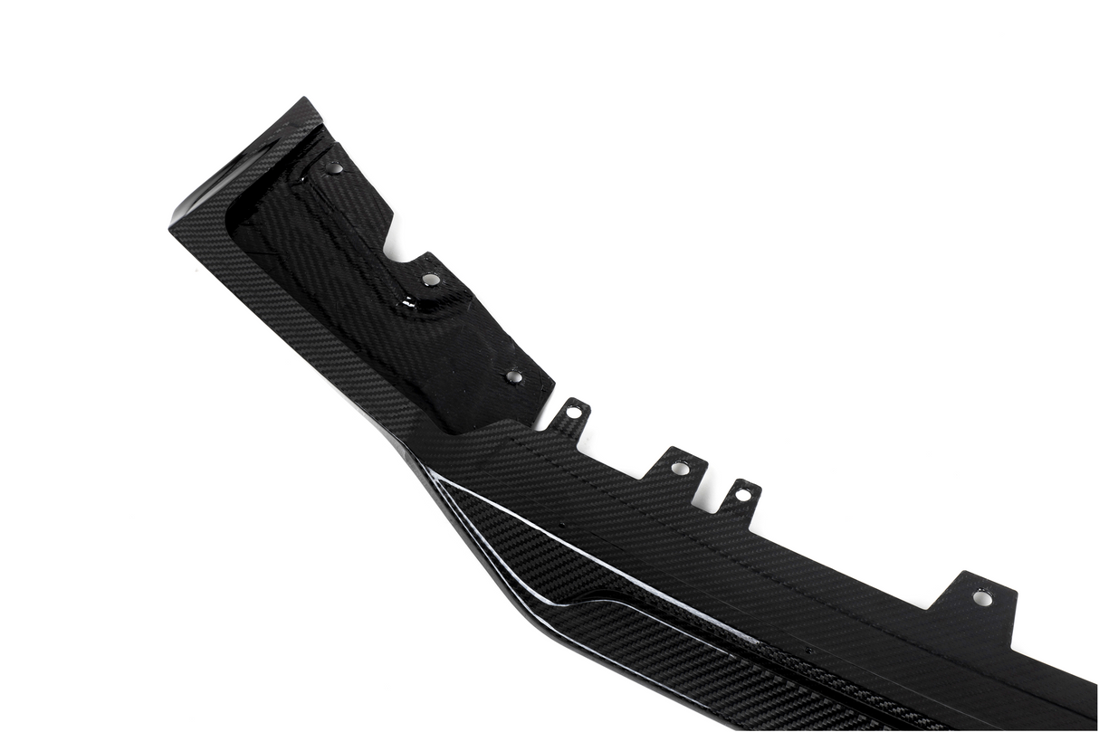 A black carbon fiber automotive component, featuring mounting points and textured patterns, lies against a plain white background.