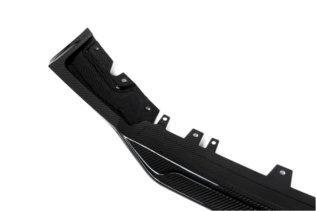 A black carbon fiber automotive component, featuring mounting points and textured patterns, lies against a plain white background.
