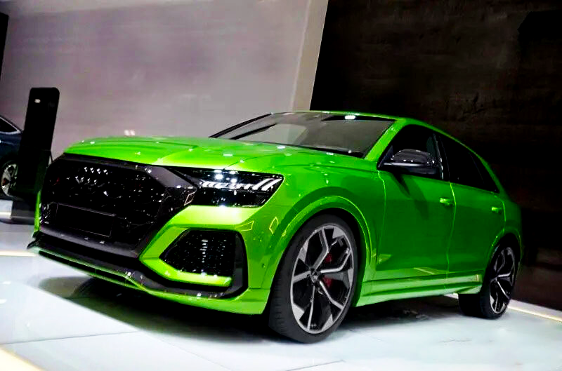 A bright green car is displayed on a showroom floor, featuring sleek design, large wheels, and a modern appearance. The setting is a well-lit indoor exhibition space.