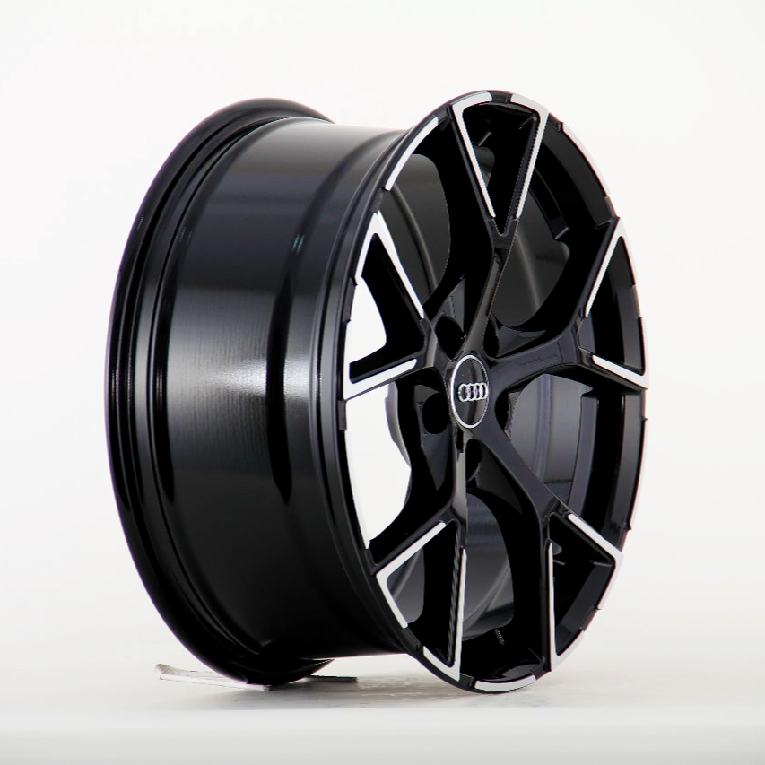 A sleek black alloy wheel with a modern, geometric design and Audi logo at the center, resting on a white surface in a studio setting.