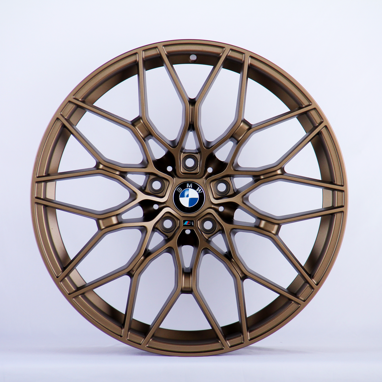 A bronze alloy wheel with intricate, multi-spoke design featuring the BMW logo in the center, set against a plain white background.