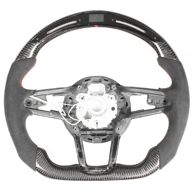 The object is a racing-style car steering wheel with carbon fiber and suede trim. The central section is unfinished, showing wiring and mounting points, against a plain white background.
