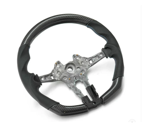 A black steering wheel with metal framework, featuring blue stitching and carbon fiber-like texture, rests on a plain white background.