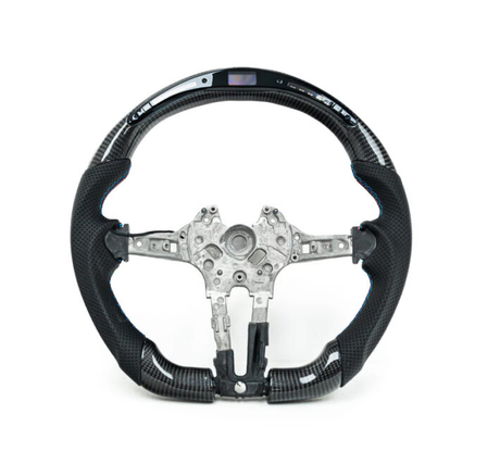 A carbon fiber steering wheel with metal interior components is displayed against a white background. Some buttons and an embedded digital display are visible on the upper section.