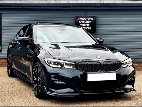 A black BMW car is parked on a paved surface in front of a gray building. A sign reads: "A6 Motors Specialist Vehicle Provider".