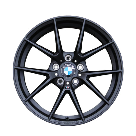 A black alloy wheel with a multi-spoke design features a BMW emblem in the center. The text "M PERFORMANCE" is written along the bottom, set against a white background.