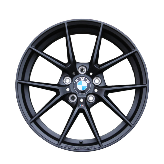 A black alloy wheel with a multi-spoke design features a BMW emblem in the center. The text "M PERFORMANCE" is written along the bottom, set against a white background.
