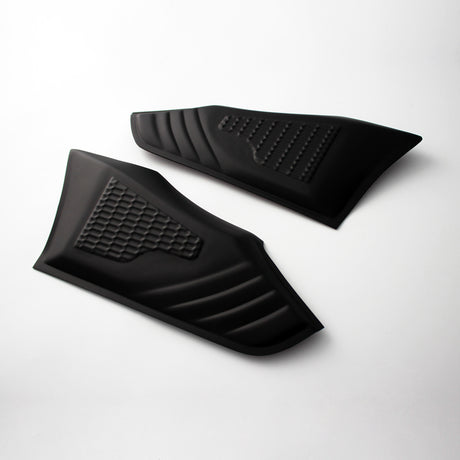 Two black rubber grip pads with textured patterns are placed on a light surface. Each pad features a distinct grid and ribbed design, typically used for vehicle or equipment grip enhancement.