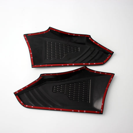 Two black plastic panels with textured surfaces, outlined by red trim tape, are positioned side by side on a plain white background.