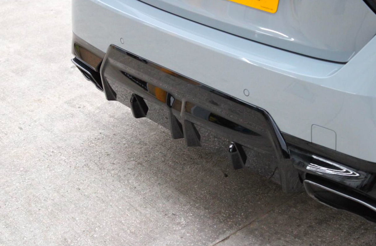 Car's rear features a glossy black diffuser with fins and exhaust openings, parked on a concrete surface. A yellow license plate is partially visible above.