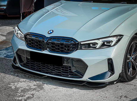 A sleek, gray BMW car's front view with a large grille and angular headlights, parked on a textured asphalt surface.