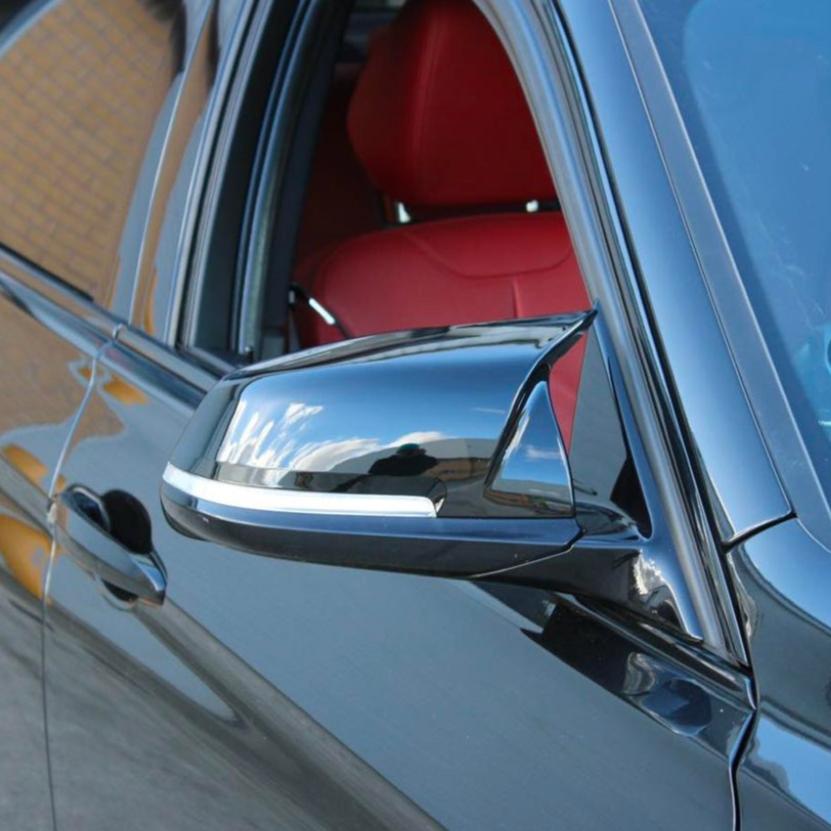 A sleek car side mirror reflects cloudy skies, attached to a black vehicle. The car's window is open, revealing a vivid red interior. The background shows a brick wall.