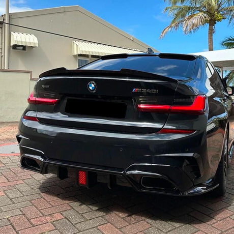 A black BMW 1340i is parked on a brick driveway. The setting includes a beige building with awnings and a palm tree under a clear blue sky.