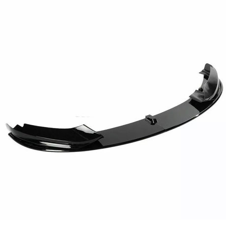 A sleek, black car front lip spoiler is resting on a plain, white background. It features a curved aerodynamic design, often used for reducing drag and enhancing vehicle performance.
