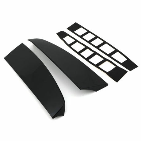 Two glossy black car spoiler pieces lay parallel, accompanied by two sets of adhesive strips with rectangular cutouts, all set against a plain white background.