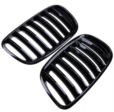 Black kidney-shaped car grilles with multiple vertical slats are placed side by side against a white background, showcasing their sleek, glossy finish.