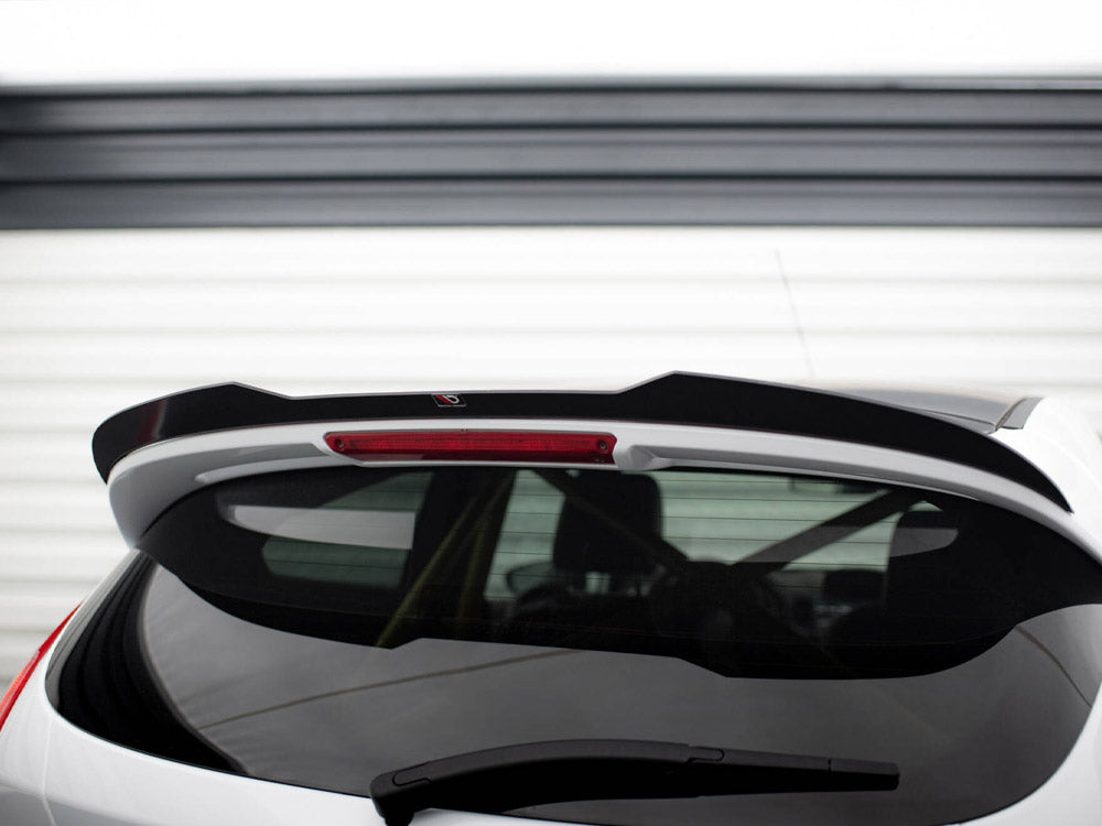 A white car's rear hatch with a black spoiler, featuring a centered red brake light, is parked in front of a white garage door with horizontal panels.