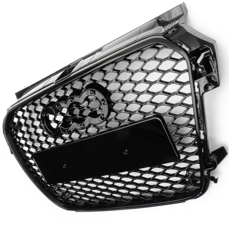 A black honeycomb grille with four interlocking rings logo is depicted. It features a rectangular plate in the center, angled against a plain white background.