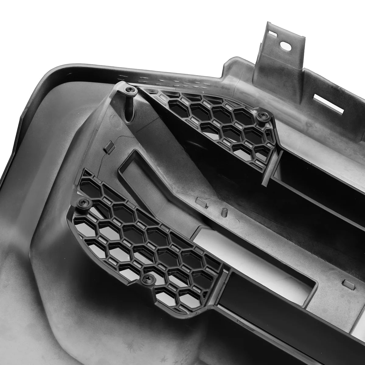 A black plastic object features honeycomb-patterned vents, viewed in close-up detail. It appears to be part of a larger structure, suggesting an automotive component in a workshop setting.