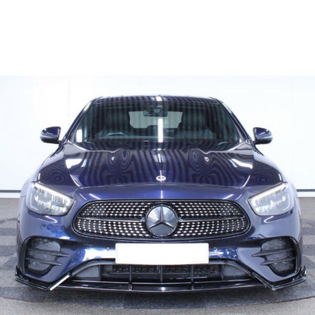 A dark blue Mercedes car is parked indoors, facing forward, highlighting its grille and emblem with a bright, reflective surface. The background is a neutral indoor setting.