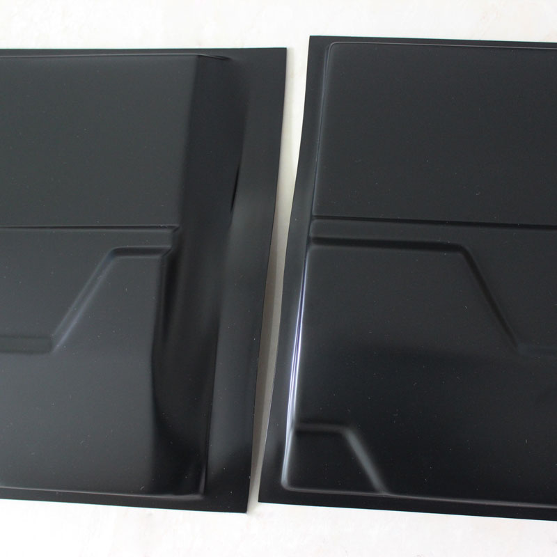 Two black metal panels lie side by side on a light surface, featuring subtle geometric indentations and smooth, reflective finishes, suggesting industrial or construction use.