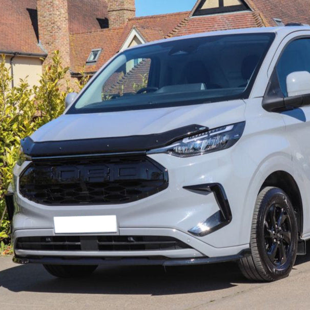 A gray van is parked on a street, displaying a sleek, modern front grille with the word "FORCE" spelled out. It's surrounded by residential buildings and greenery.
