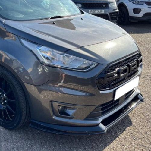 A dark gray car with a modern design is parked on asphalt, featuring a distinctive black grille with the letters "FOD." Other parked cars are visible in the background.