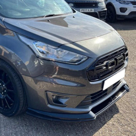 A dark gray car with a modern design is parked on asphalt, featuring a distinctive black grille with the letters "FOD." Other parked cars are visible in the background.