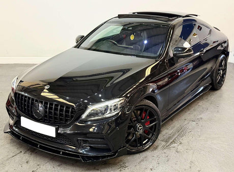 A black Mercedes-Benz coupe with an open sunroof is parked indoors. It features a sleek design, AMG wheels with red brake calipers, and a smiley face air freshener inside.
