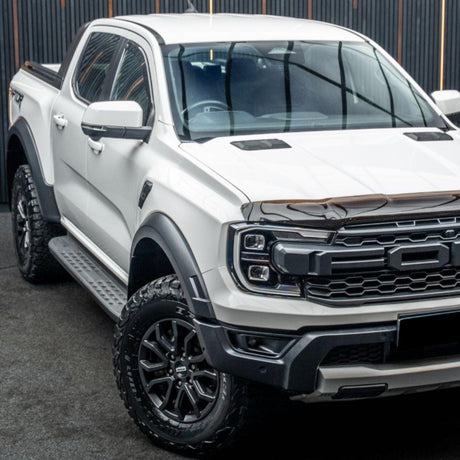 White pickup truck parked inside a building, displaying a bold grille and rugged tires. The backdrop features dark vertical panels, creating a contrasting modern industrial atmosphere.