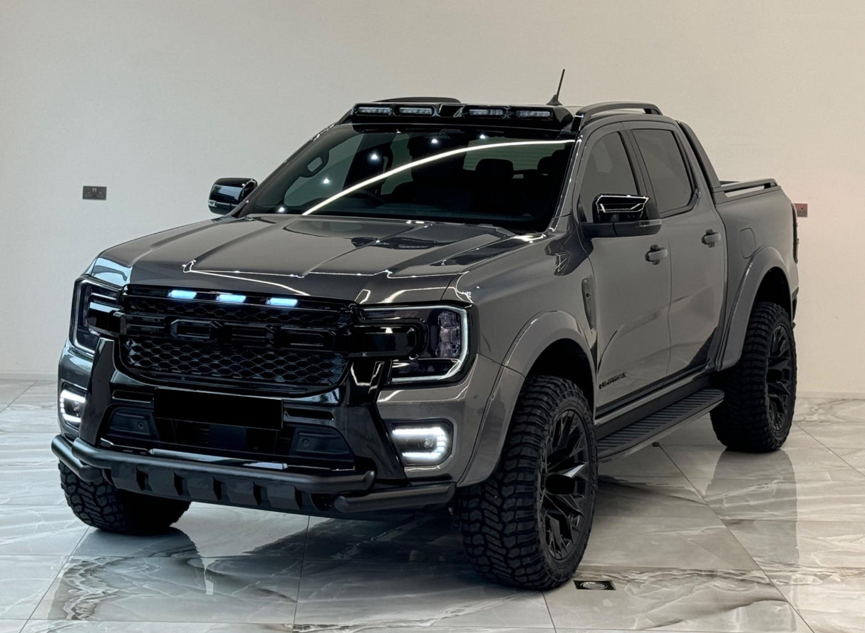 A dark gray pickup truck with rugged tires and LED lights is parked indoors on a polished tiled floor, under bright overhead lighting, showcasing a modern design.