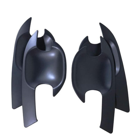 Two black, abstract chair-like objects with curved and pointed features stand upright against a plain white background, resembling stylized sculpture or modern art pieces.