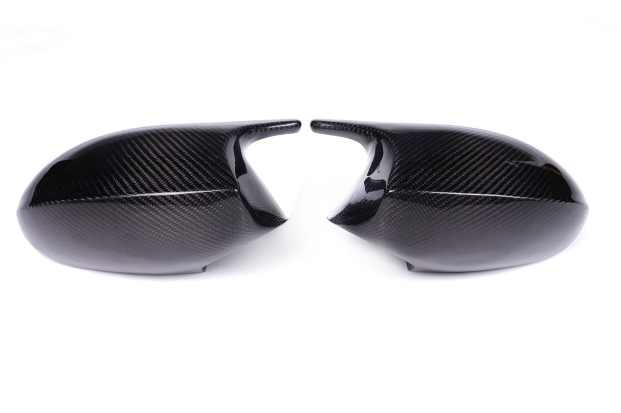 Two carbon fiber car mirror covers face each other against a plain white background, displaying a sleek, glossy surface with a distinct woven pattern.