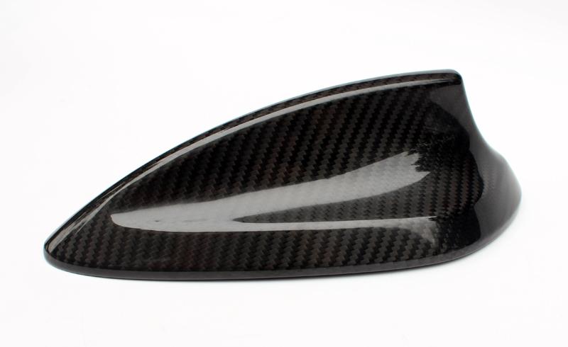 A carbon fiber shark fin antenna lies on a white background, displaying a sleek, aerodynamic design with a glossy, patterned surface.