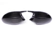Two black carbon fiber car mirror covers face each other, resting on a plain white background, highlighting their glossy texture and sleek design.