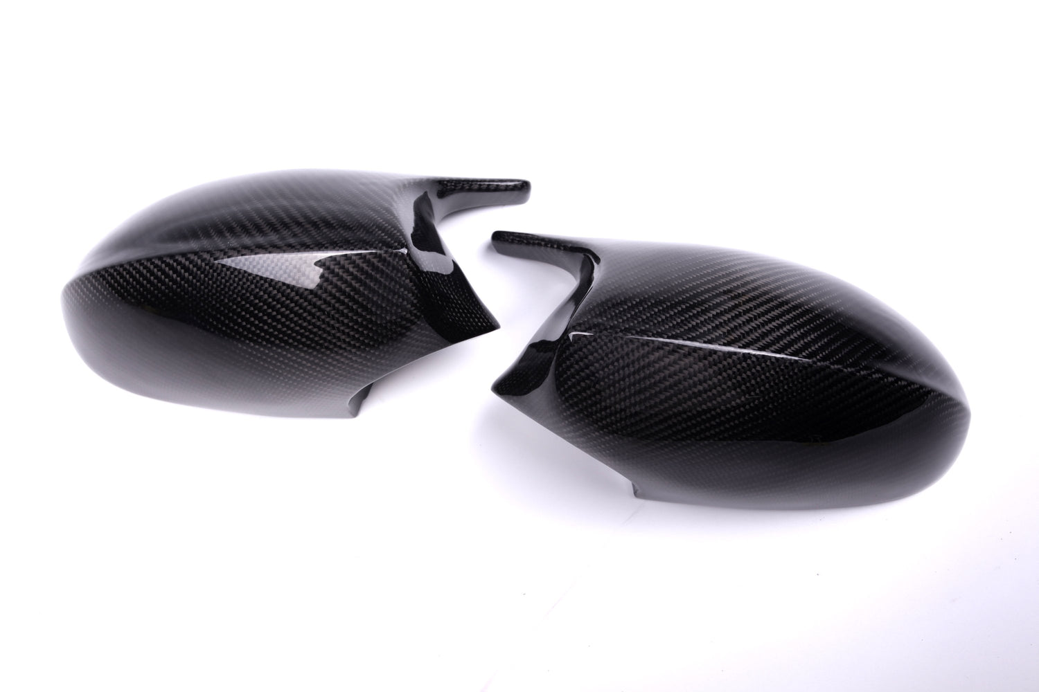 Two sleek carbon fiber side mirror covers, positioned facing each other, rest against a plain white background. Their dark, glossy surface highlights the distinctive carbon fiber texture.