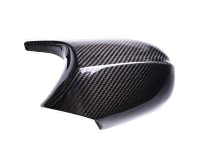 Carbon fiber car mirror cover resting at an angle, displaying intricate woven pattern; reflective surface highlighted by bright studio lighting against a plain white background.