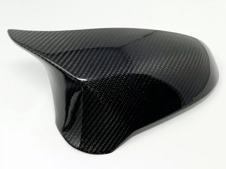 A smooth, glossy carbon fiber piece rests against a plain white background, showcasing its sleek, curved design and textured pattern, likely used as a protective cover or aerodynamic component.