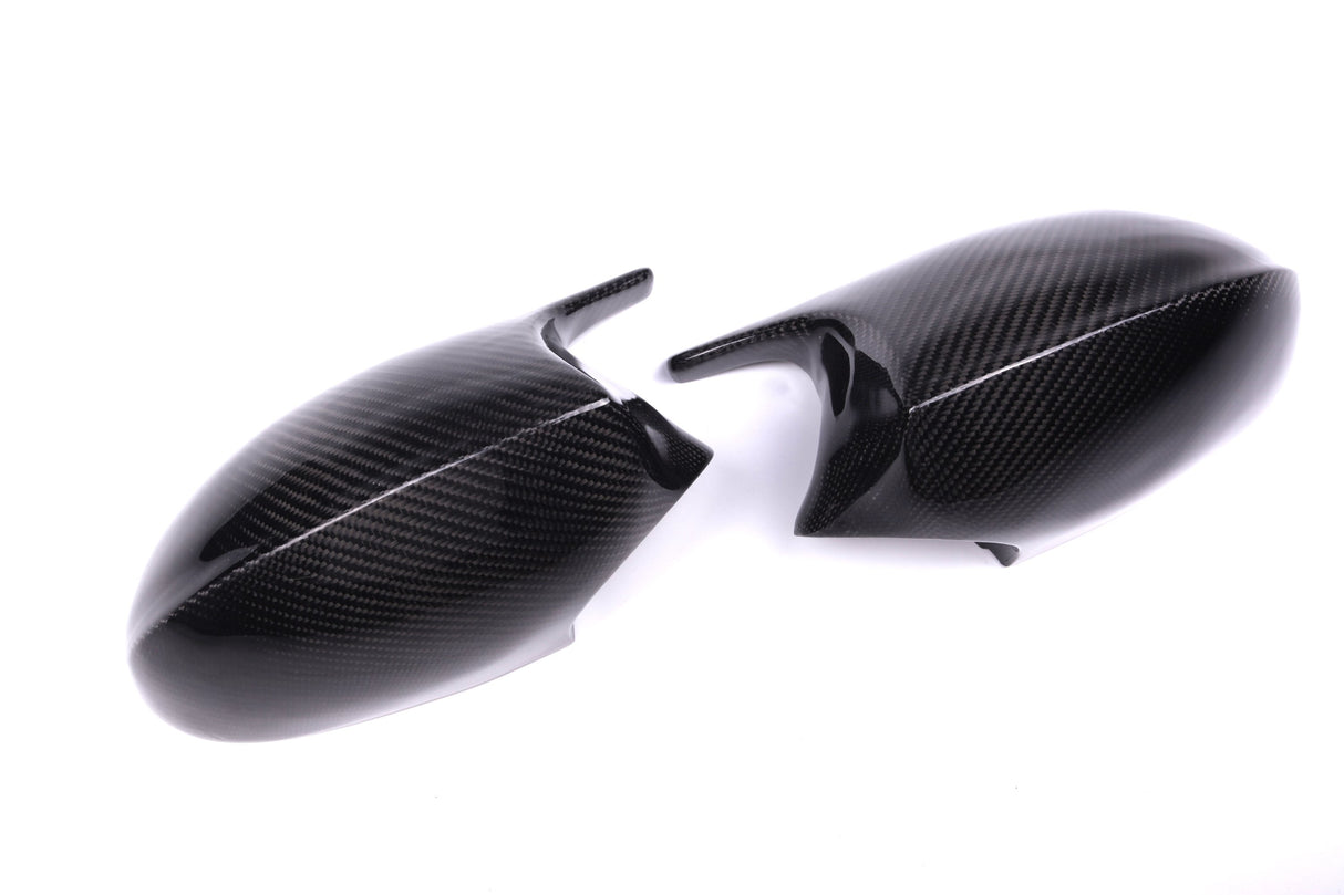 Two carbon fiber car side mirror covers lie on a white surface, displaying a sleek, glossy texture and a subtle weave pattern.