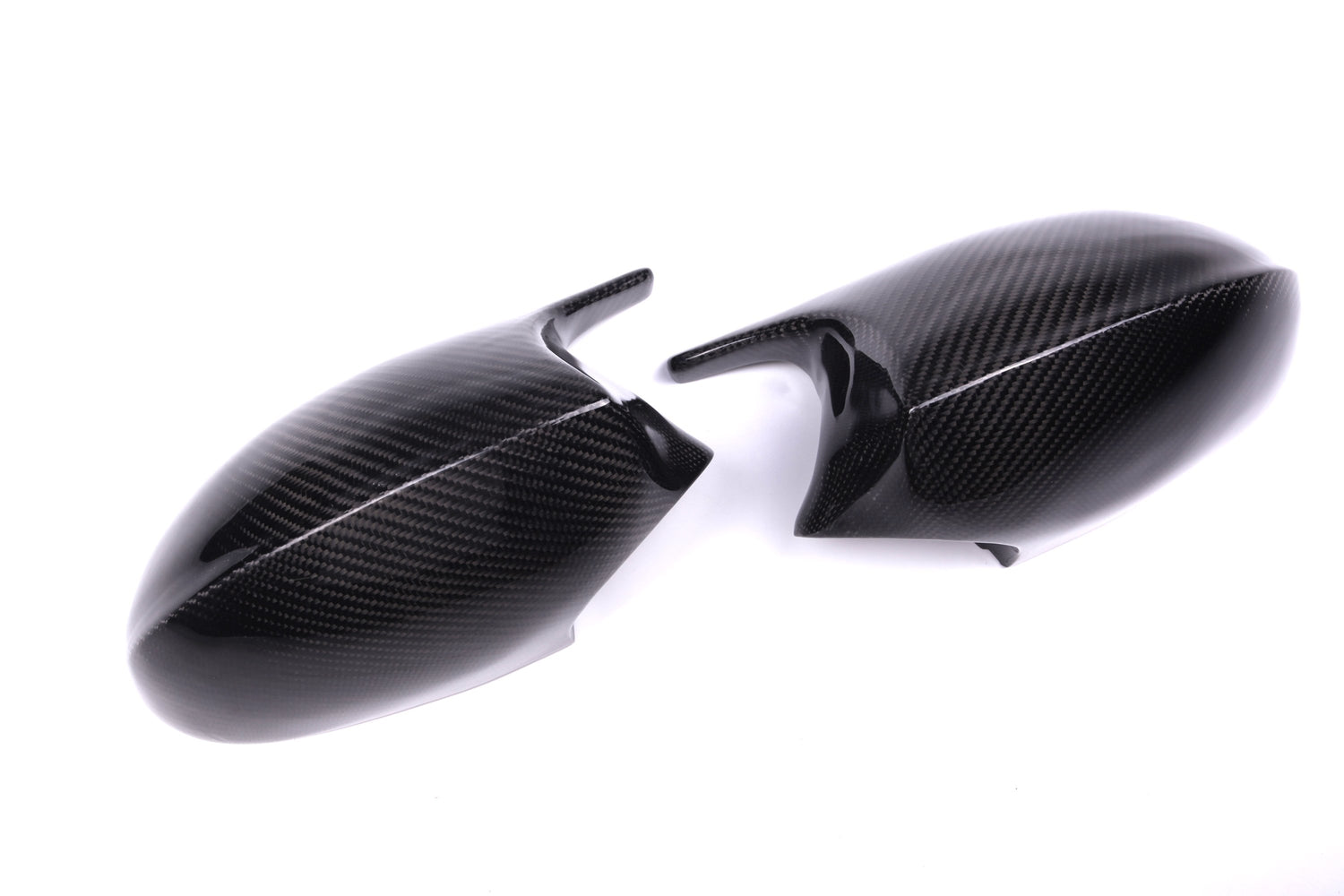 Two carbon fiber car side mirror covers lie on a white surface, displaying a sleek, glossy texture and a subtle weave pattern.