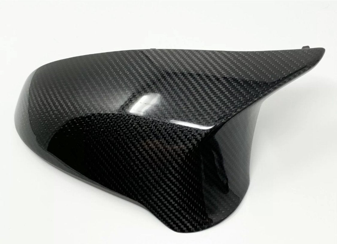 A glossy, black carbon fiber car mirror cover rests on a plain white background, its surface reflecting light with a distinctive woven pattern.