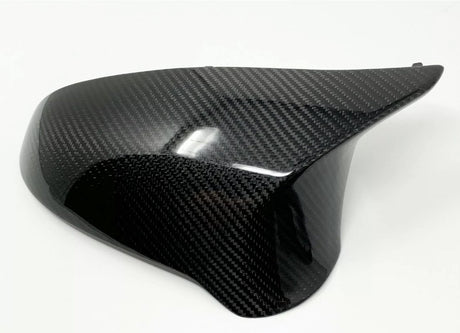 A glossy, black carbon fiber car mirror cover rests on a plain white background, its surface reflecting light with a distinctive woven pattern.