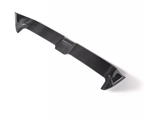 A carbon fiber car spoiler lies on a plain white background, highlighting its aerodynamic shape and texture.