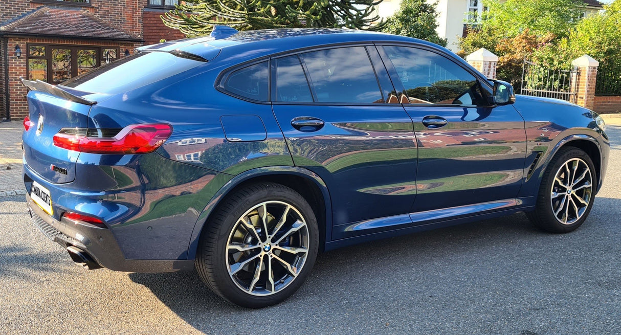 A blue car is parked on a residential street, featuring sleek design and alloy wheels. Brick houses and green foliage surround the scene. The license plate reads "LUMMA ACCENTS."